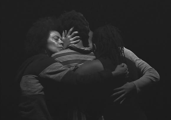 Three adults embrace in darkness