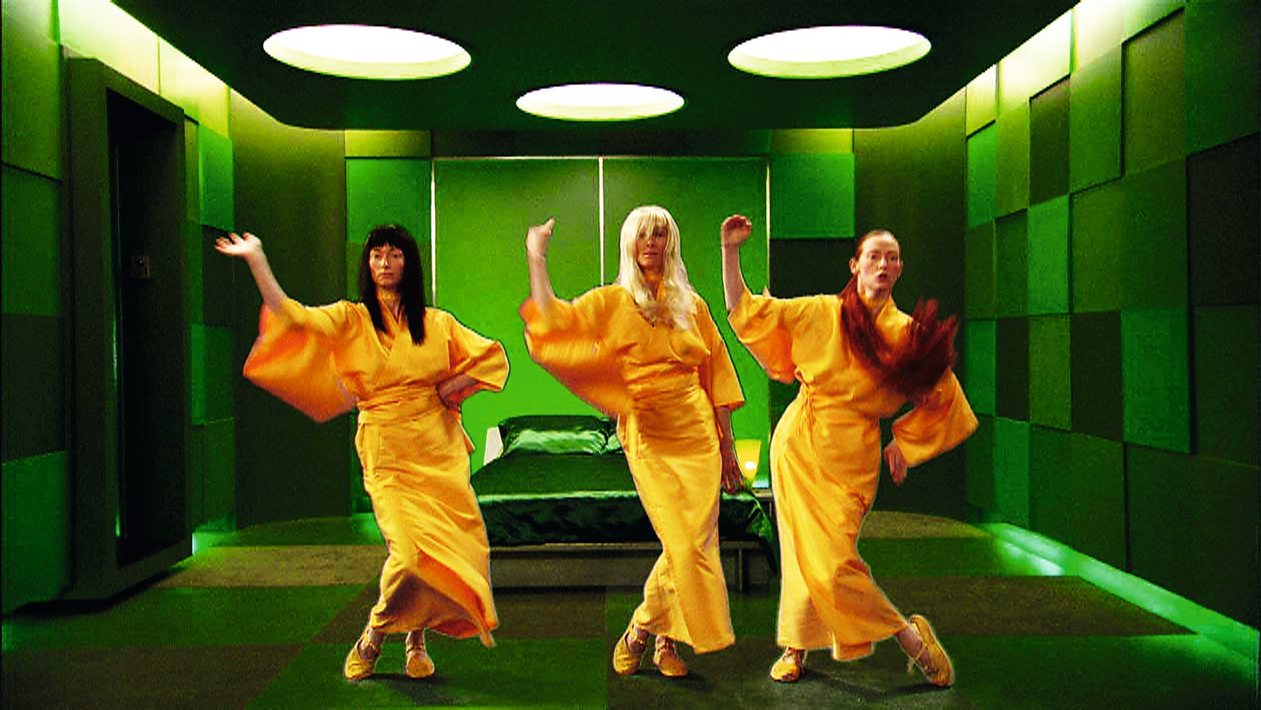 Three women wearing yellow dresses posing in a green room.