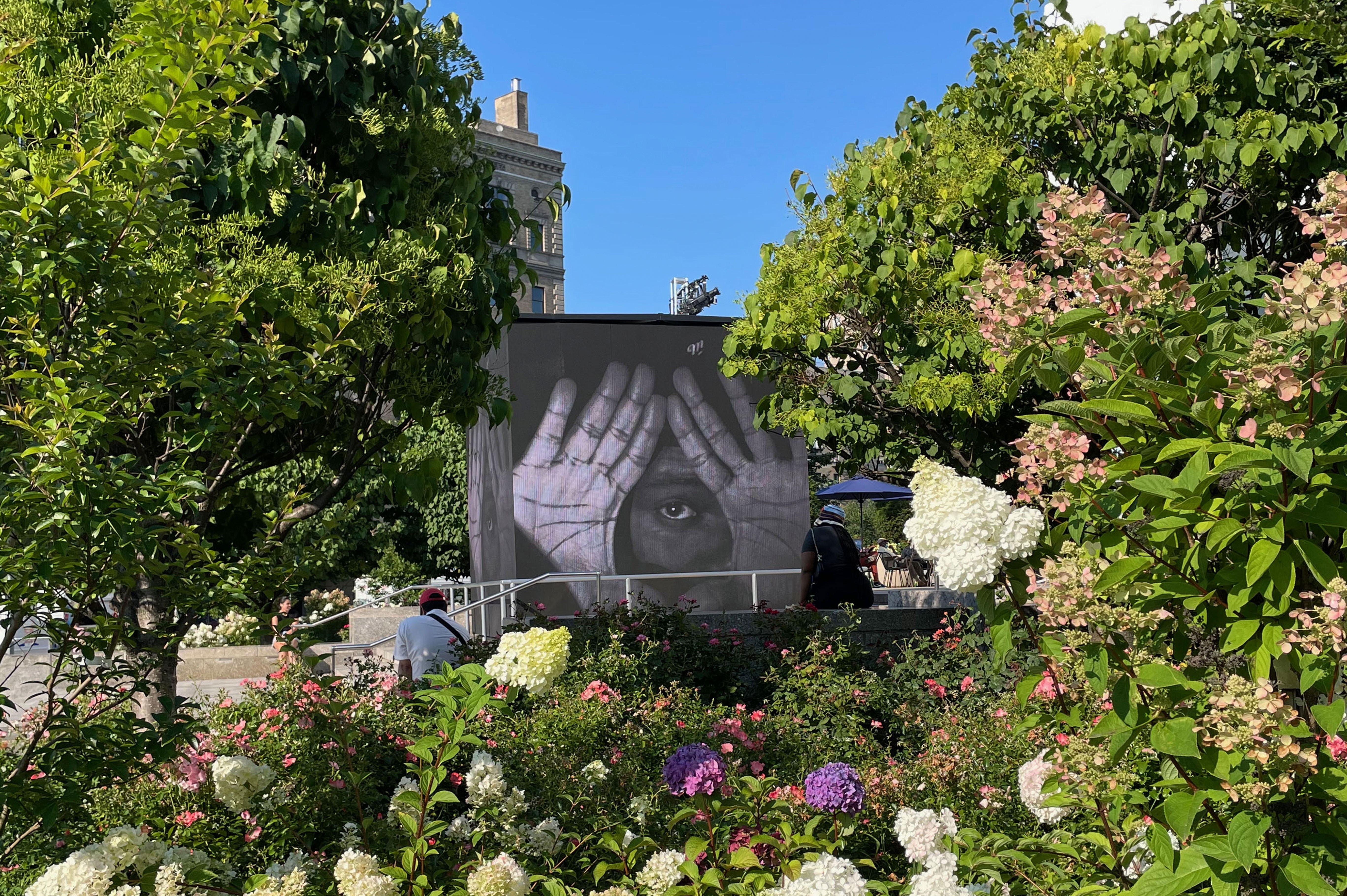 A garden with a food truck behind some trees with a mural of hands and eye.