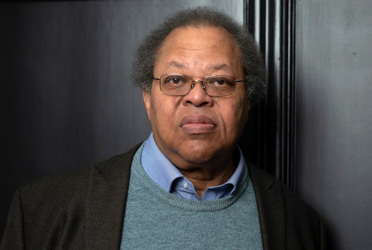 Photo of man wearing grey sweater and black coat in front of dark wall
