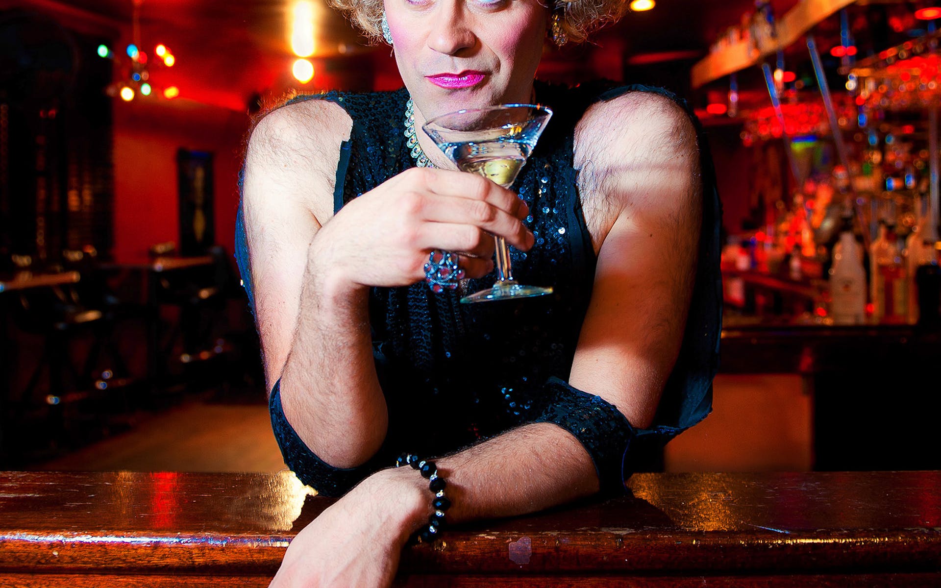 Cross dressed woman in a bar holding drink.