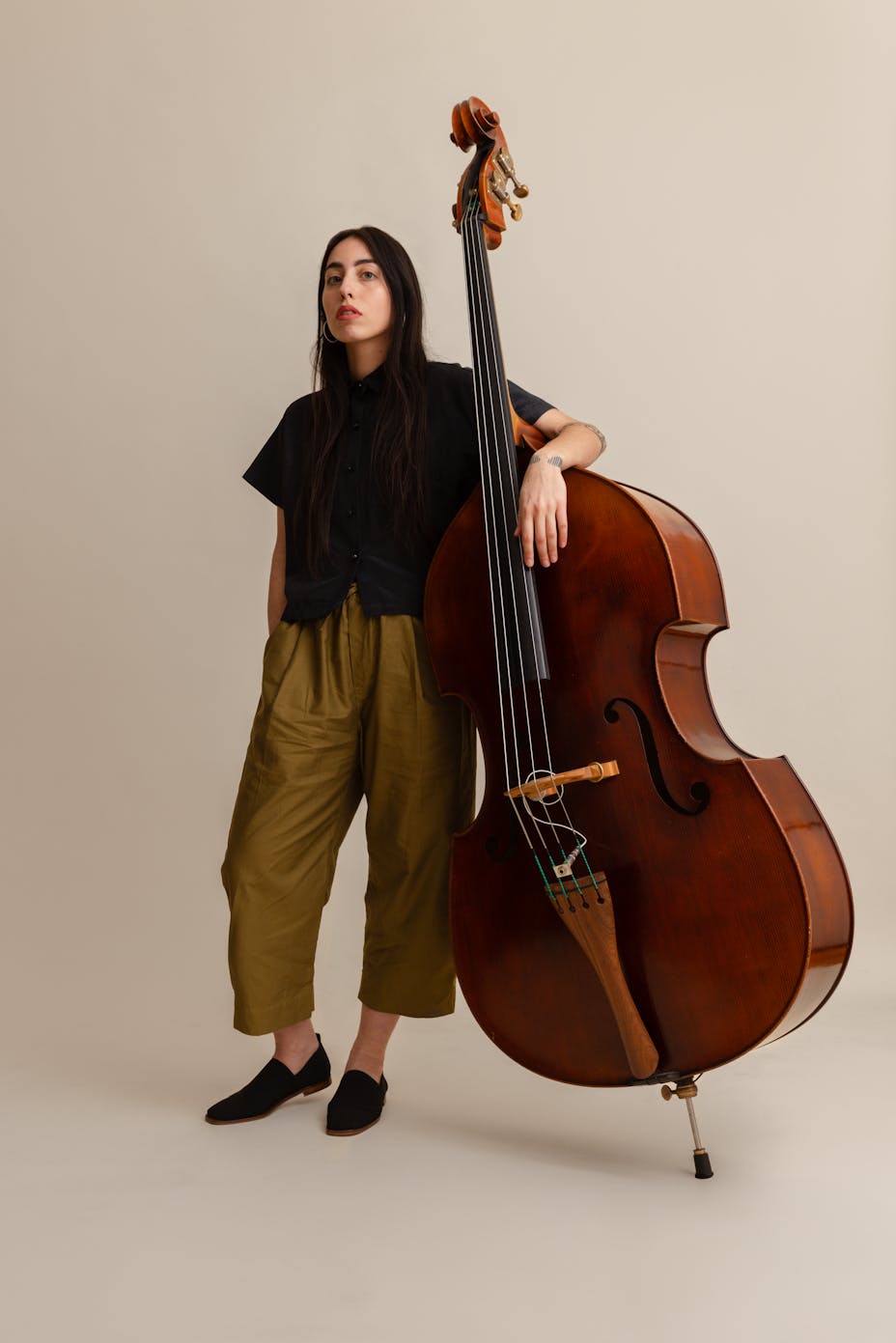 A light-skinned woman with long dark hair poses with a cello against a white background.