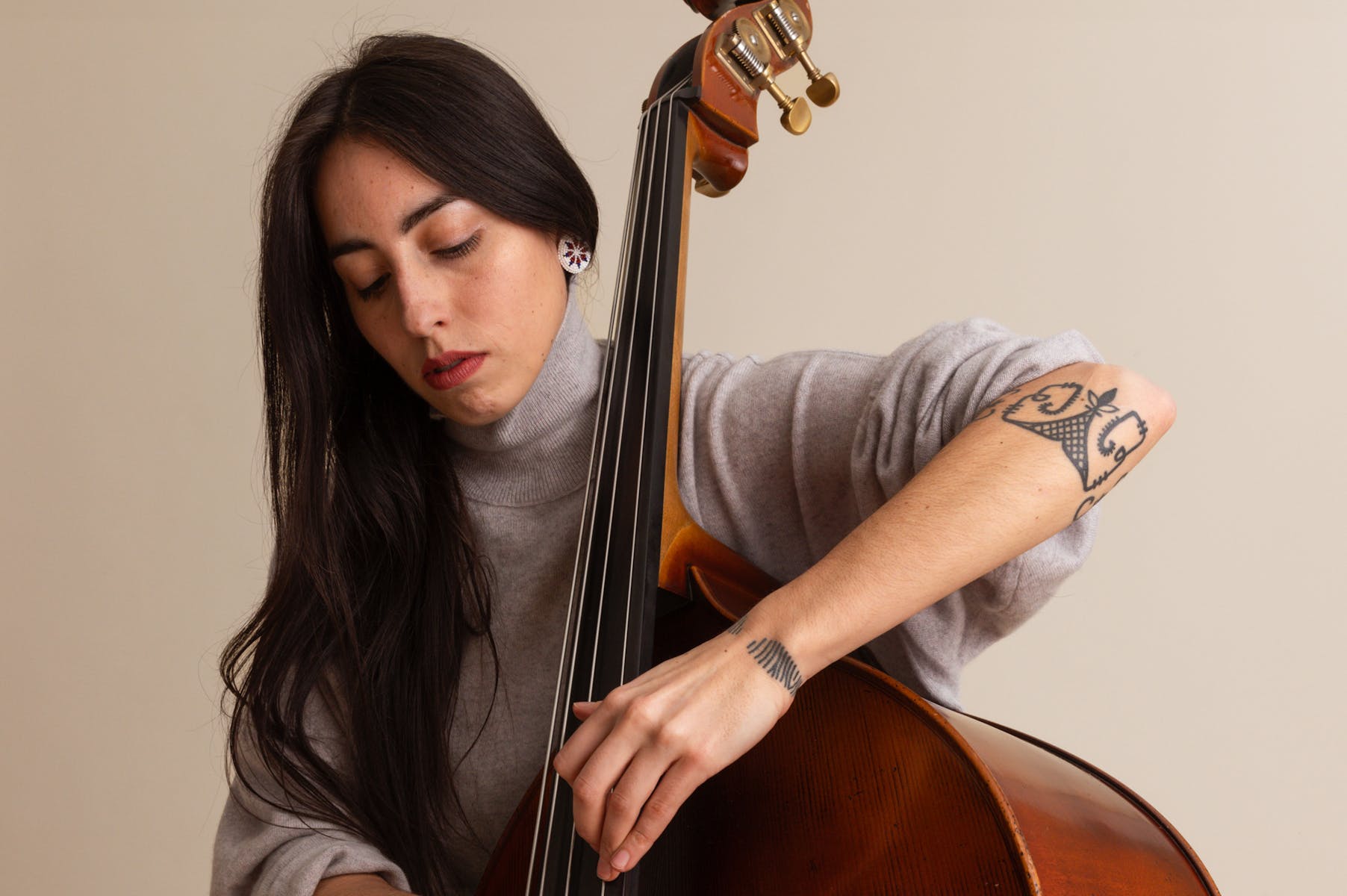 A light-skinned woman with long dark brown hair holds a cello.