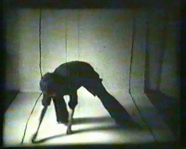 Grainy black and white film still of figure leaning over and touching the ground