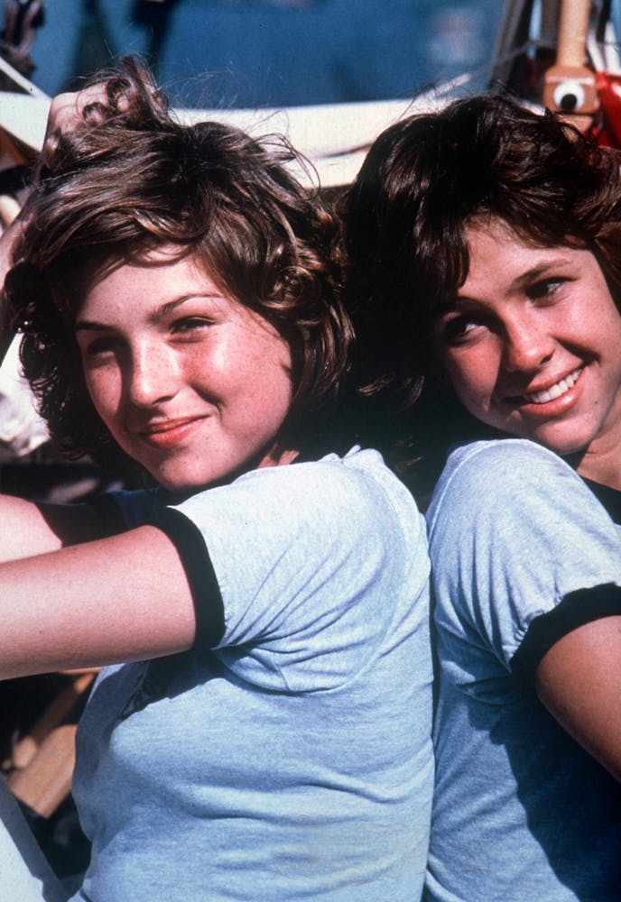 Two teenage girls smiling and sitting back to back.