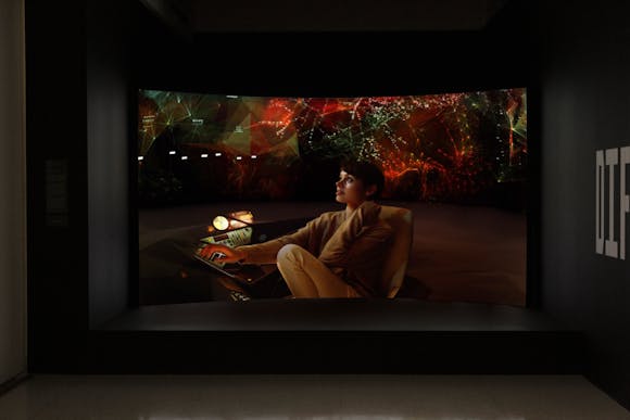 A curved video screen with a futuristic image of a woman sitting at a desk with a projection in the background