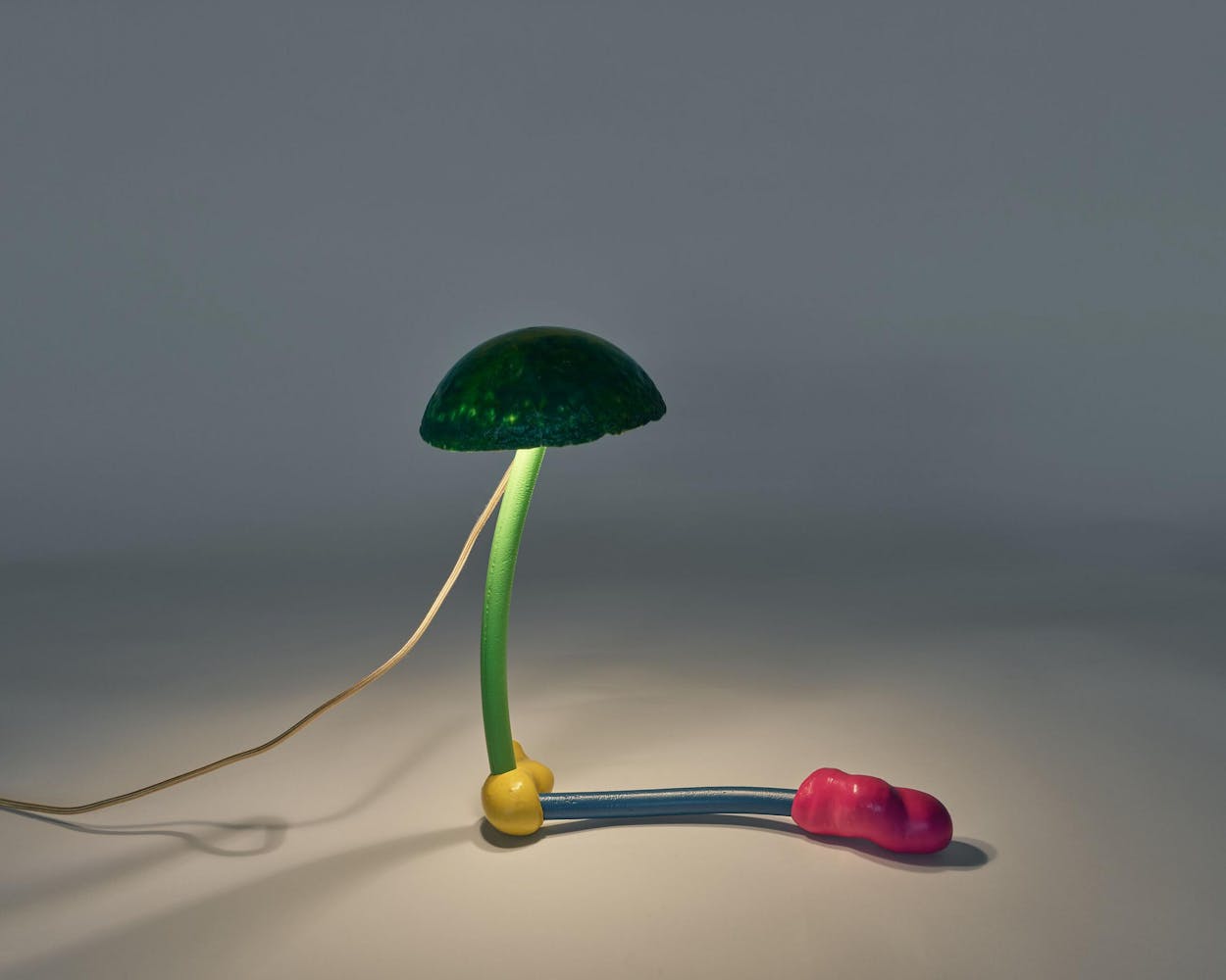 a whimsical L-shaped plastic lamp with a rounded, dark green spherical lampshade atop a bright green cylinder and abstract yellow, blue, and pink bottom.
