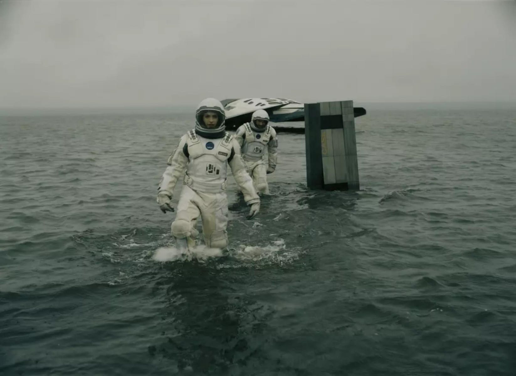 Two astronauts wade in knee-deep water that makes up the entire landscape. The walk away from a spaceship in the distance.