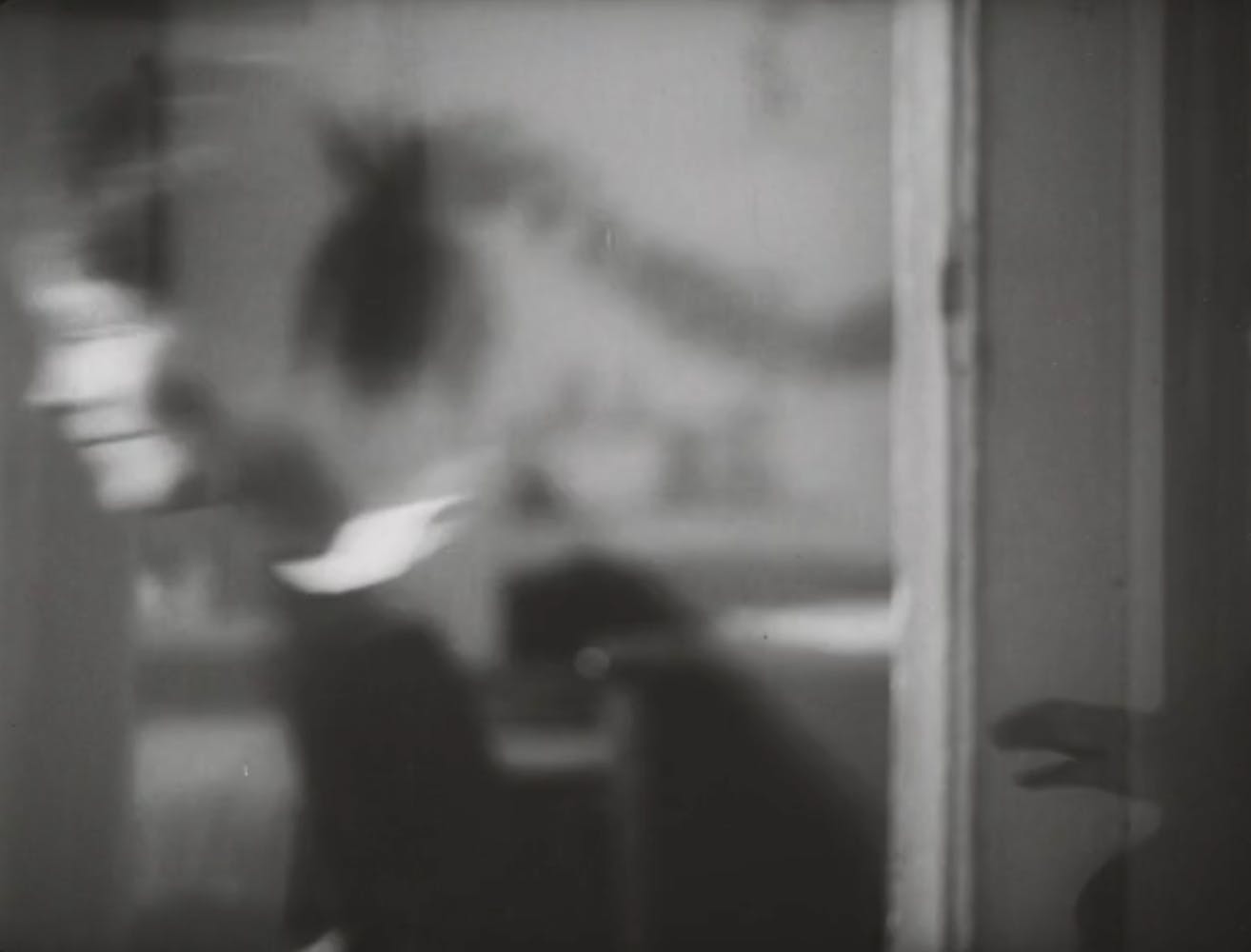 The blurred flection of a woman with light skin moving can be seen in a window.