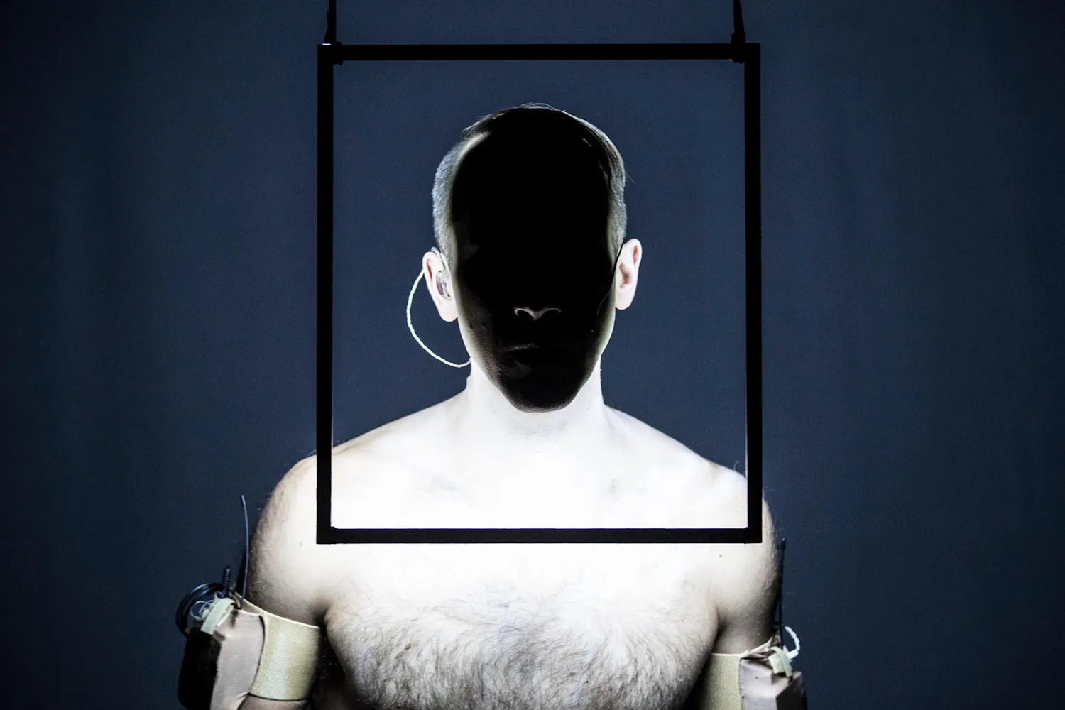 A man's face is in darkness while a glowing frame illuminates his neck and shoulders.