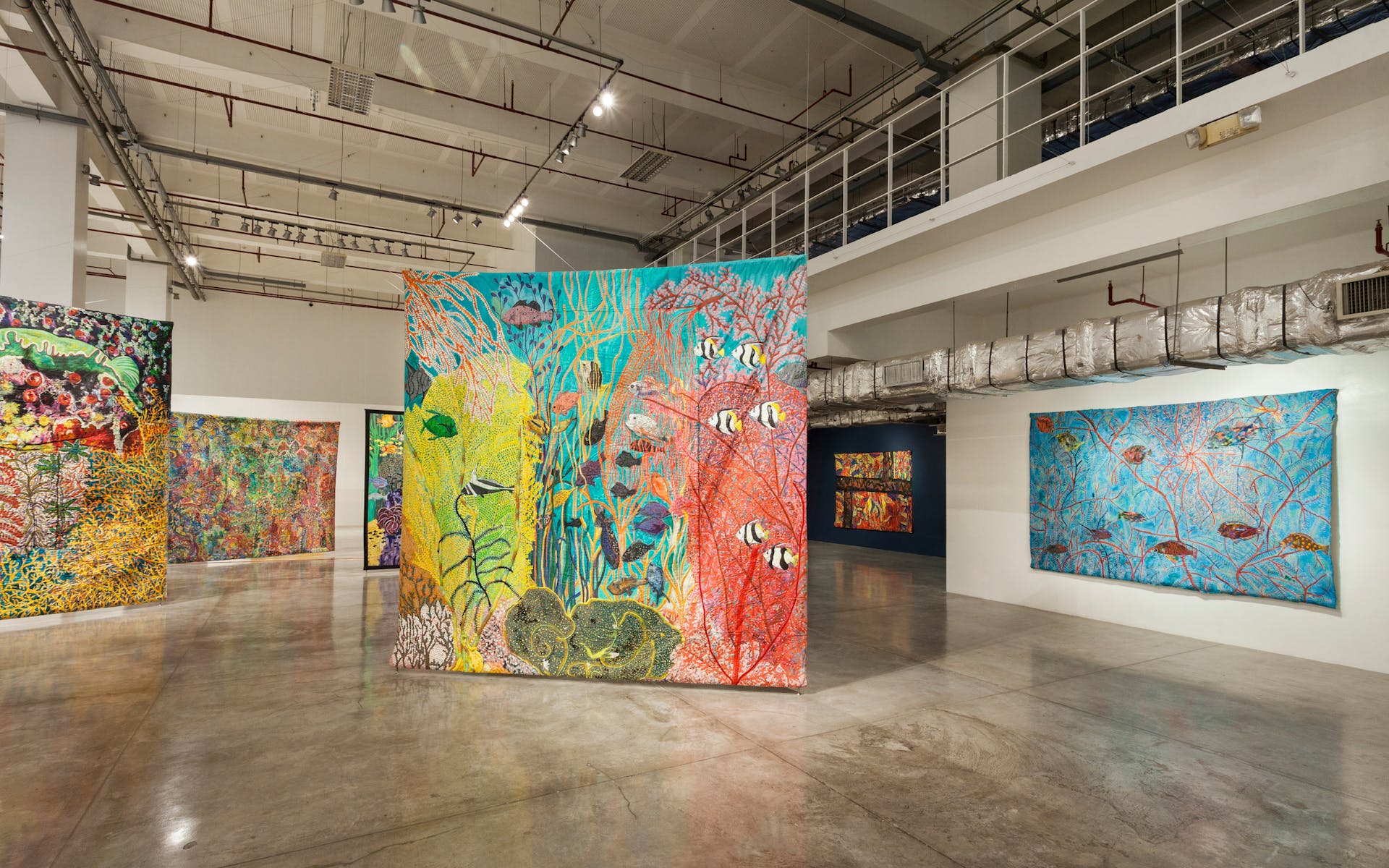 Large textile works hang in a gallery.