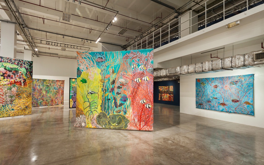 Large textile works hang in a gallery.