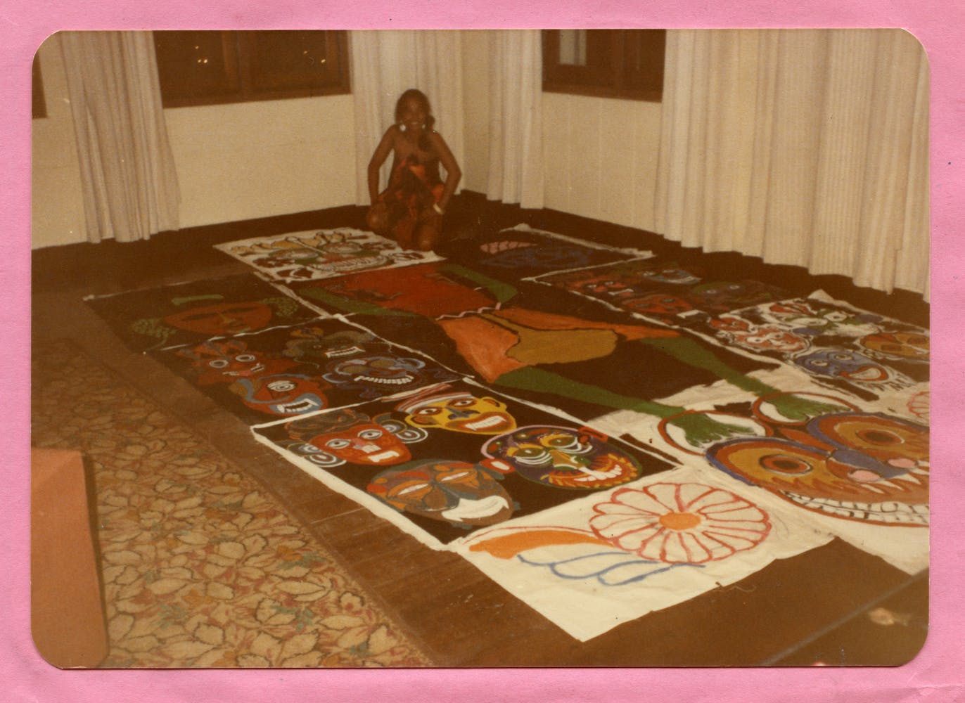 An adult woman kneels on the floor and smiles at the viewer in front of a large drawing composed of several panels.