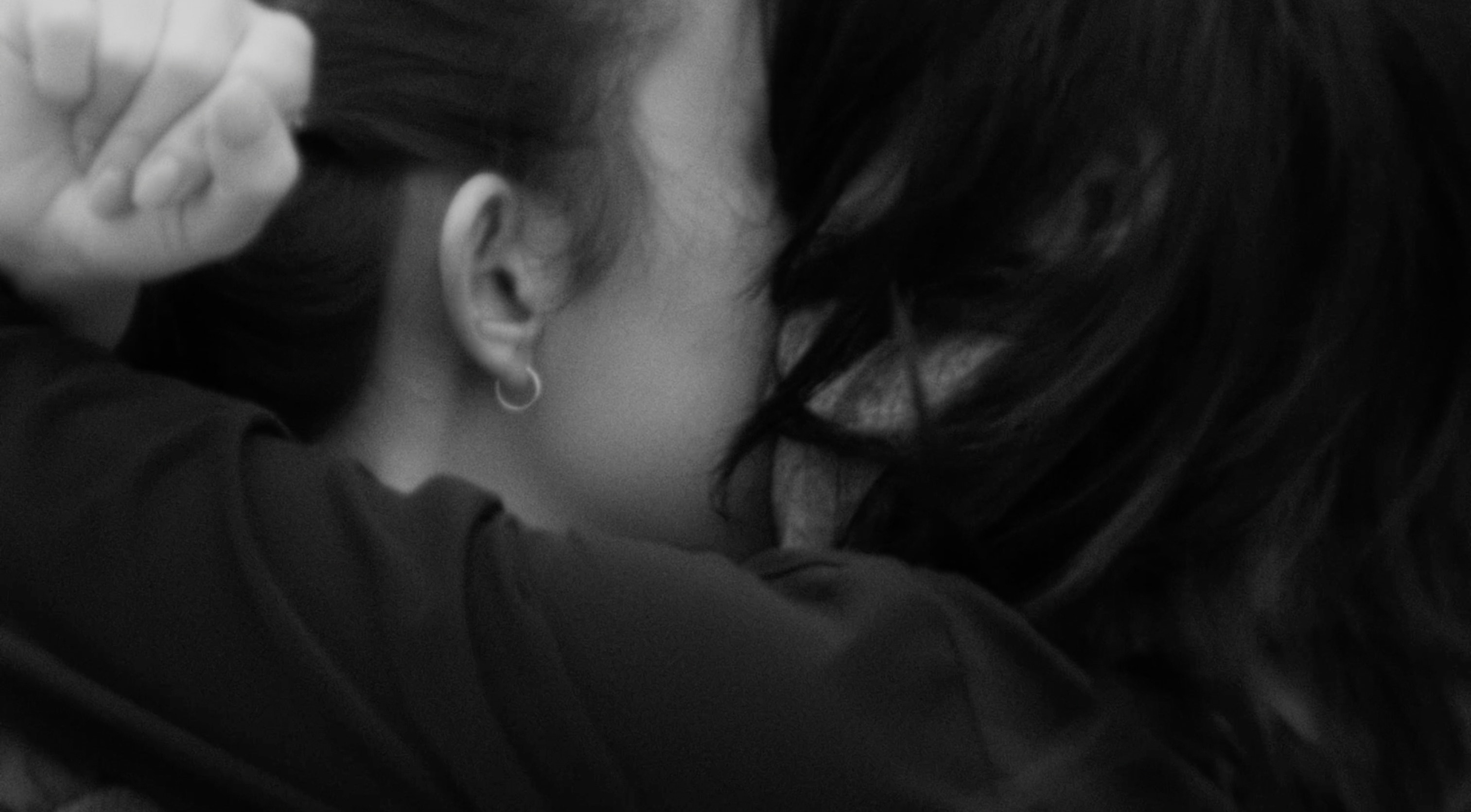 A black and white film still shows a detail of two people embracing.