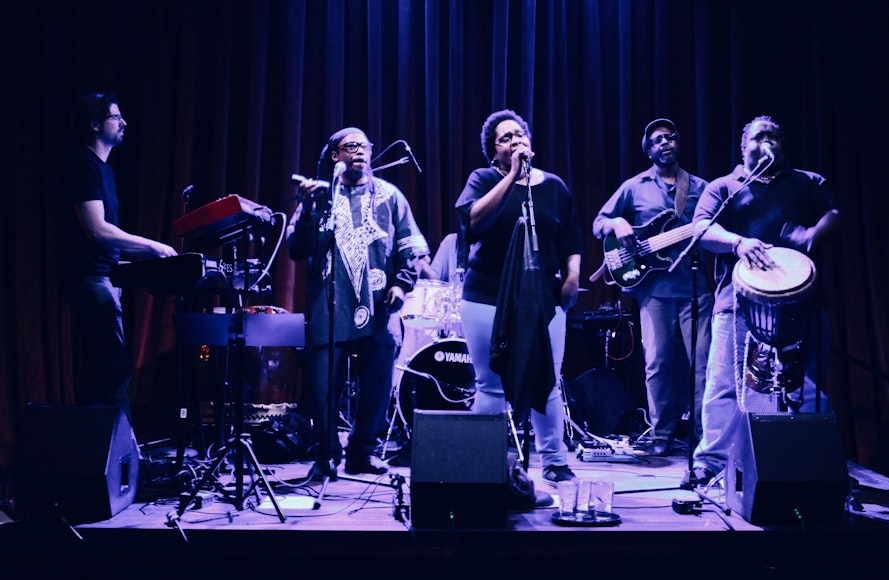 Image of five members of a band on stage bathed in blue light