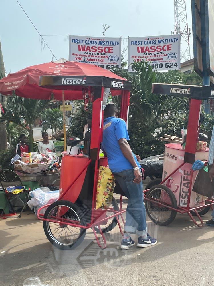 A man learns against a fruit card outside on a sunny day.