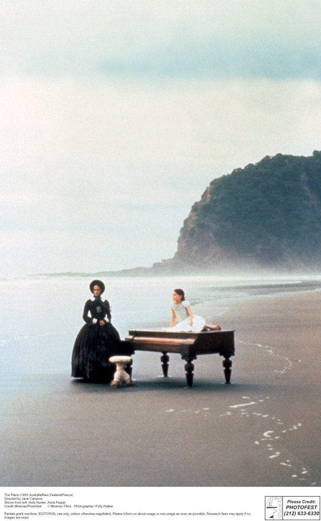 A woman sits at a piano on a beach.