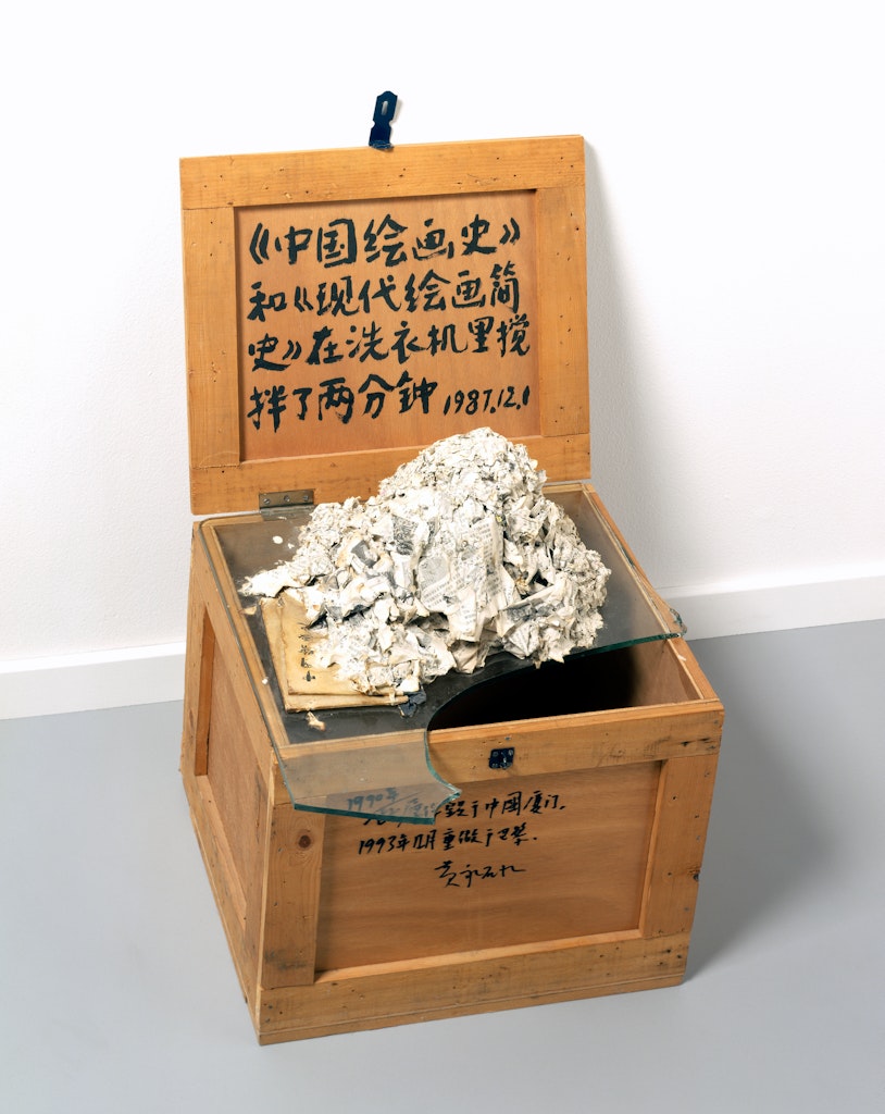 Photo of mixed media sculpture of a washing machine destroyed book on broken glass on top of a wooden crate.