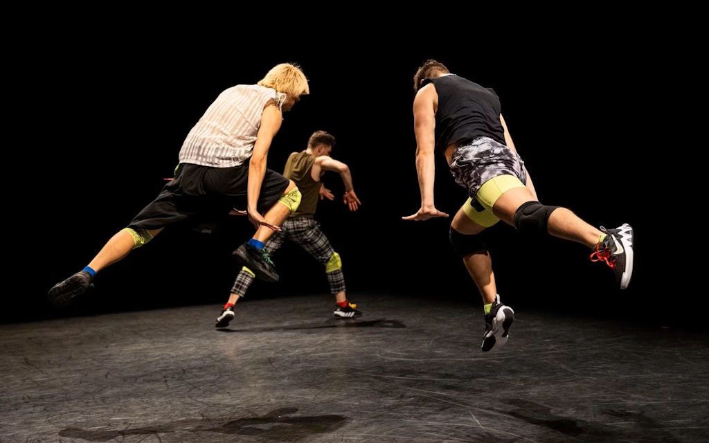 Three adults, mid pose in a dance on a black stage
