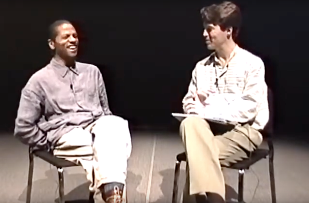 Two adults sit on chairs in a blurry photo, in mid converstaion