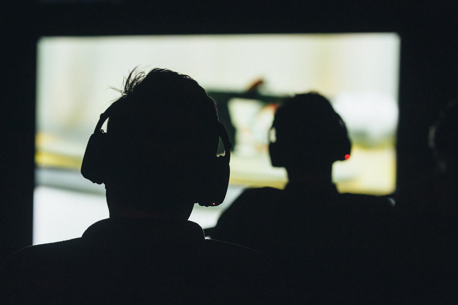 Two people wear headphones and watch a video projection.