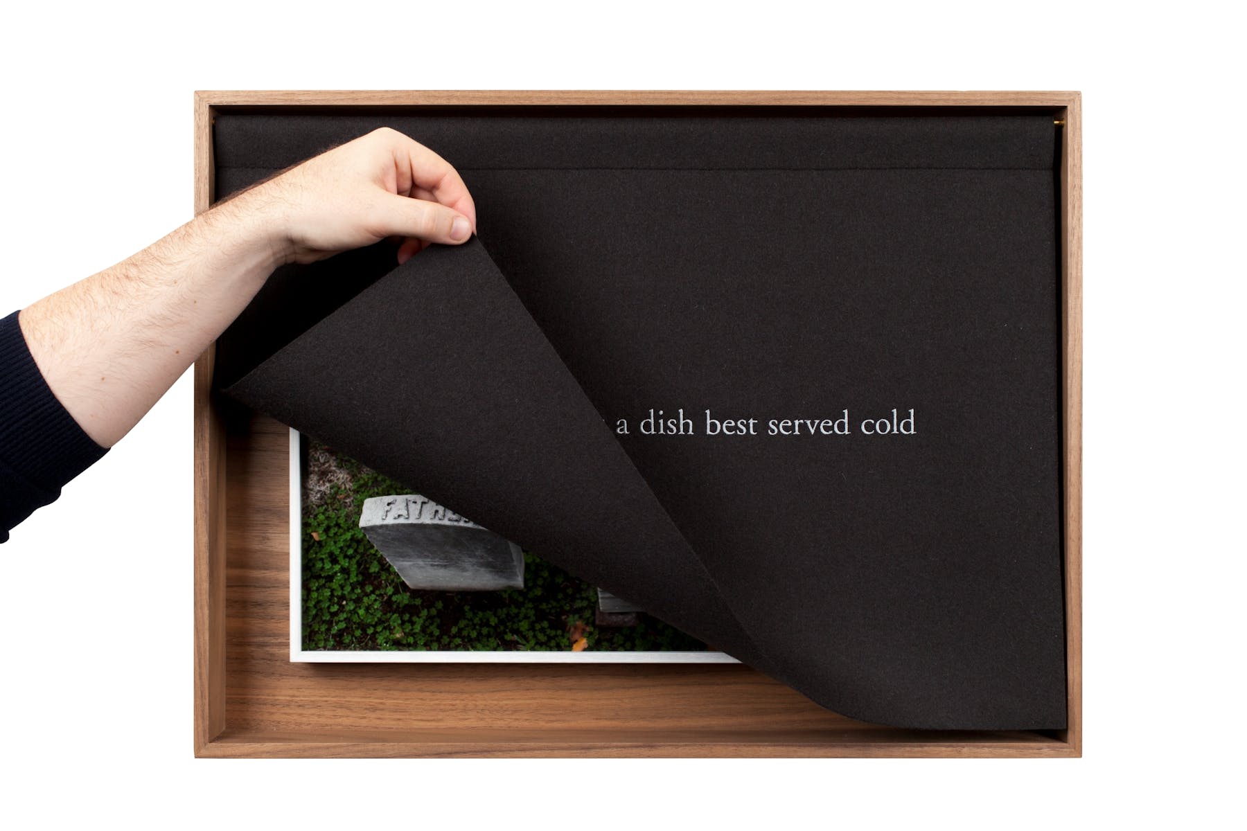 A light skinned hand lifts up a black cloth with white text covering artwork centered in a frame.