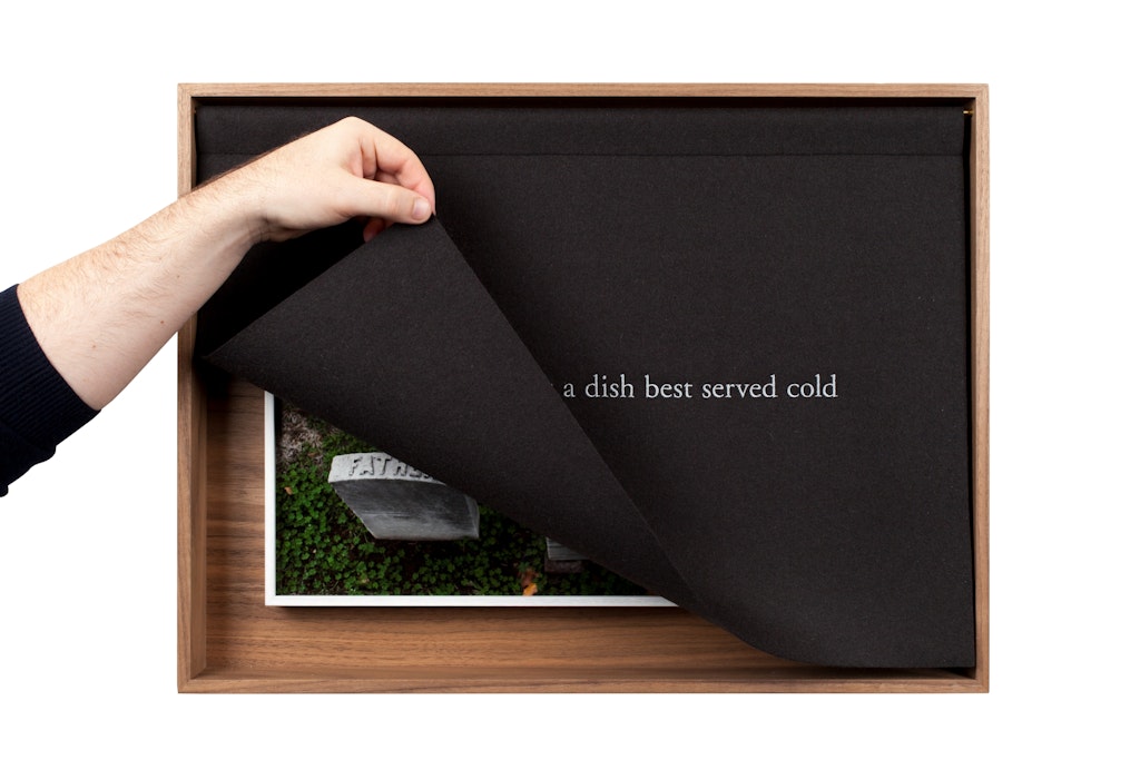 A light skinned hand lifts up a black cloth with white text covering artwork centered in a frame.