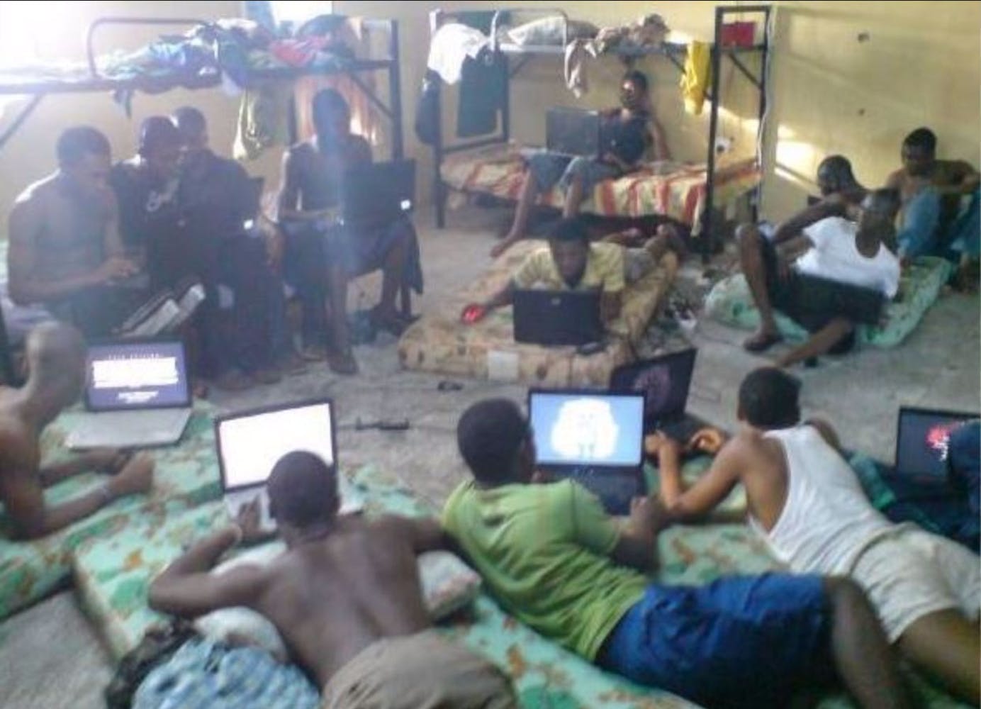 A group of adult lie on the ground and sit in chairs in a small room while all working on their laptops