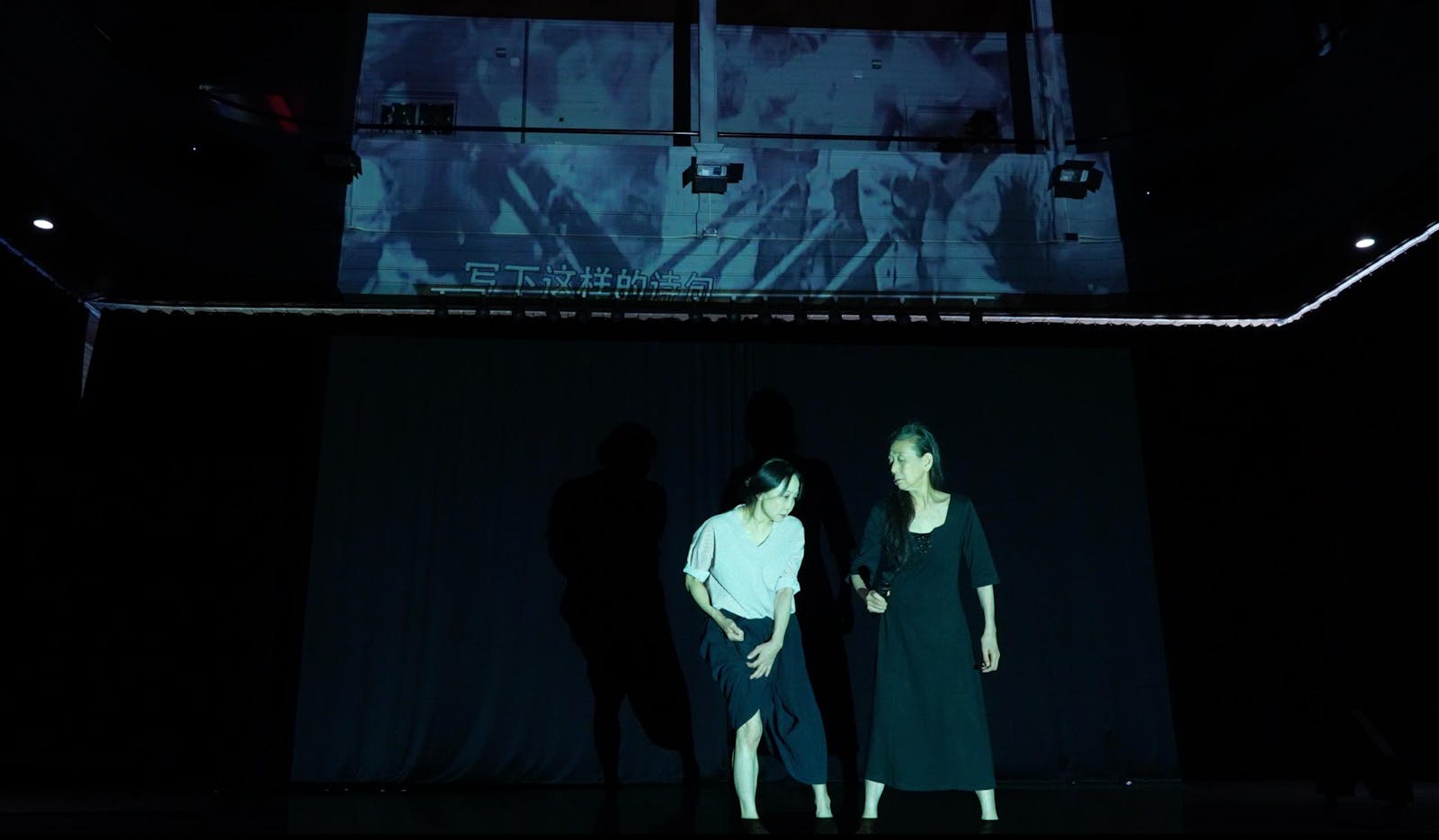 Two performers with medium skin dance in front of a projection on the wall.