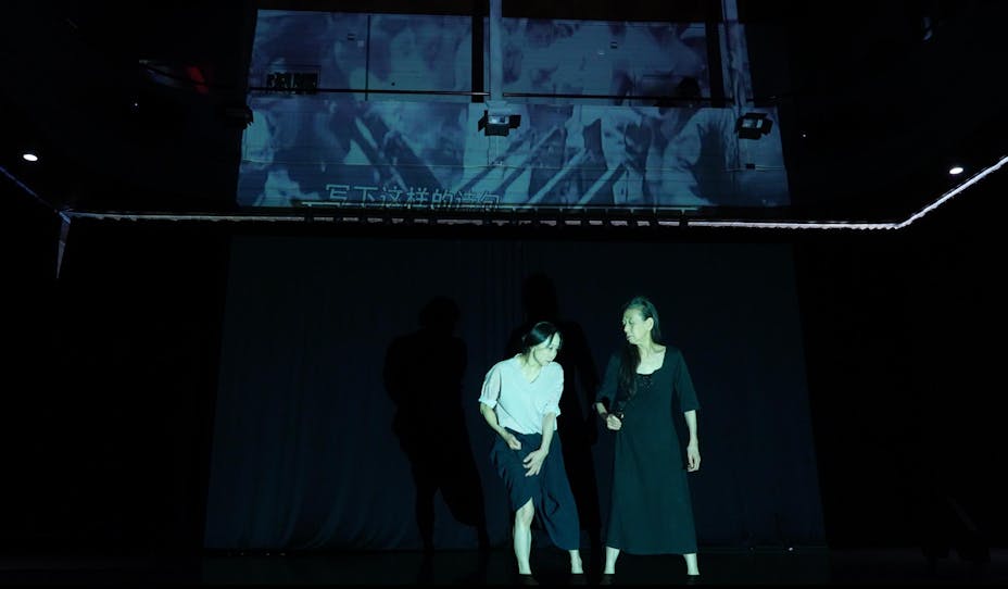 Two performers with medium skin dance in front of a projection on the wall.