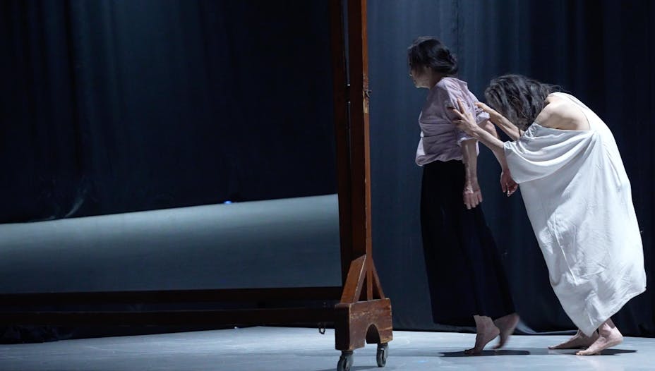 One performer with medium skin holds another's arms behind them.