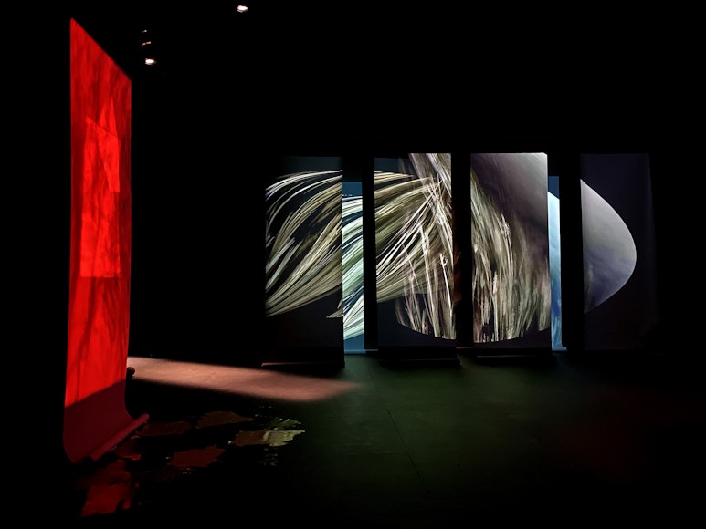 A dark space with light swirling around columns and a red wall on the left.