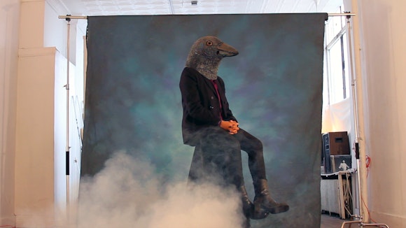 Image of person wearing crow mask with smoke in the foreground
