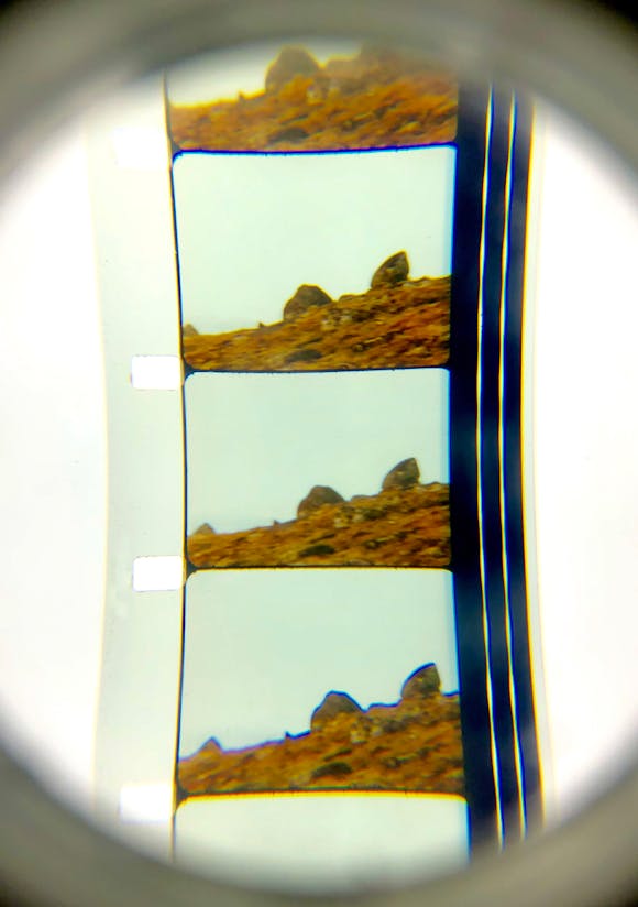 Film strip under a magnifying loop depicting multiple frames of a rocky hill