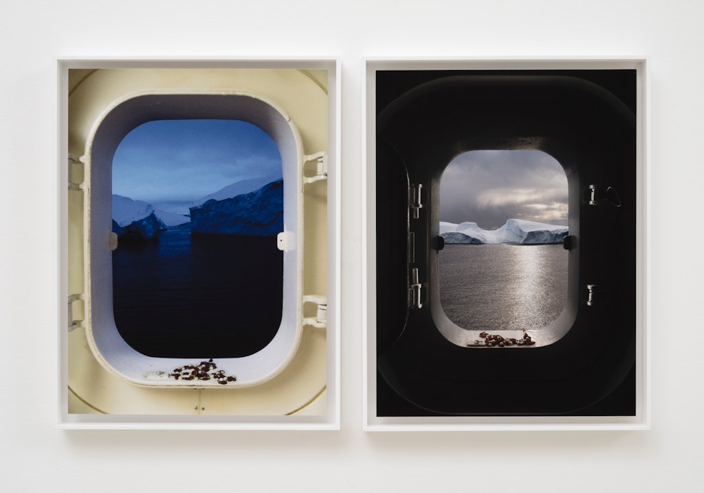 Two ship porthole windows show icy seascapes with icebergs, one at dusk and one in daylight.