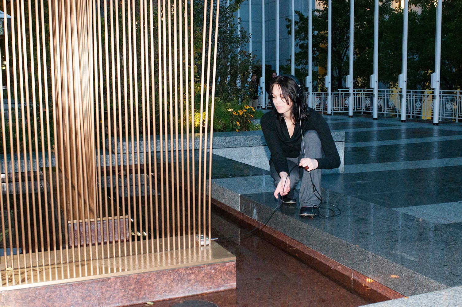 Woman leaning over metal sculpture listing to headphones.