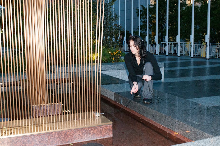 Woman leaning over metal sculpture listing to headphones.