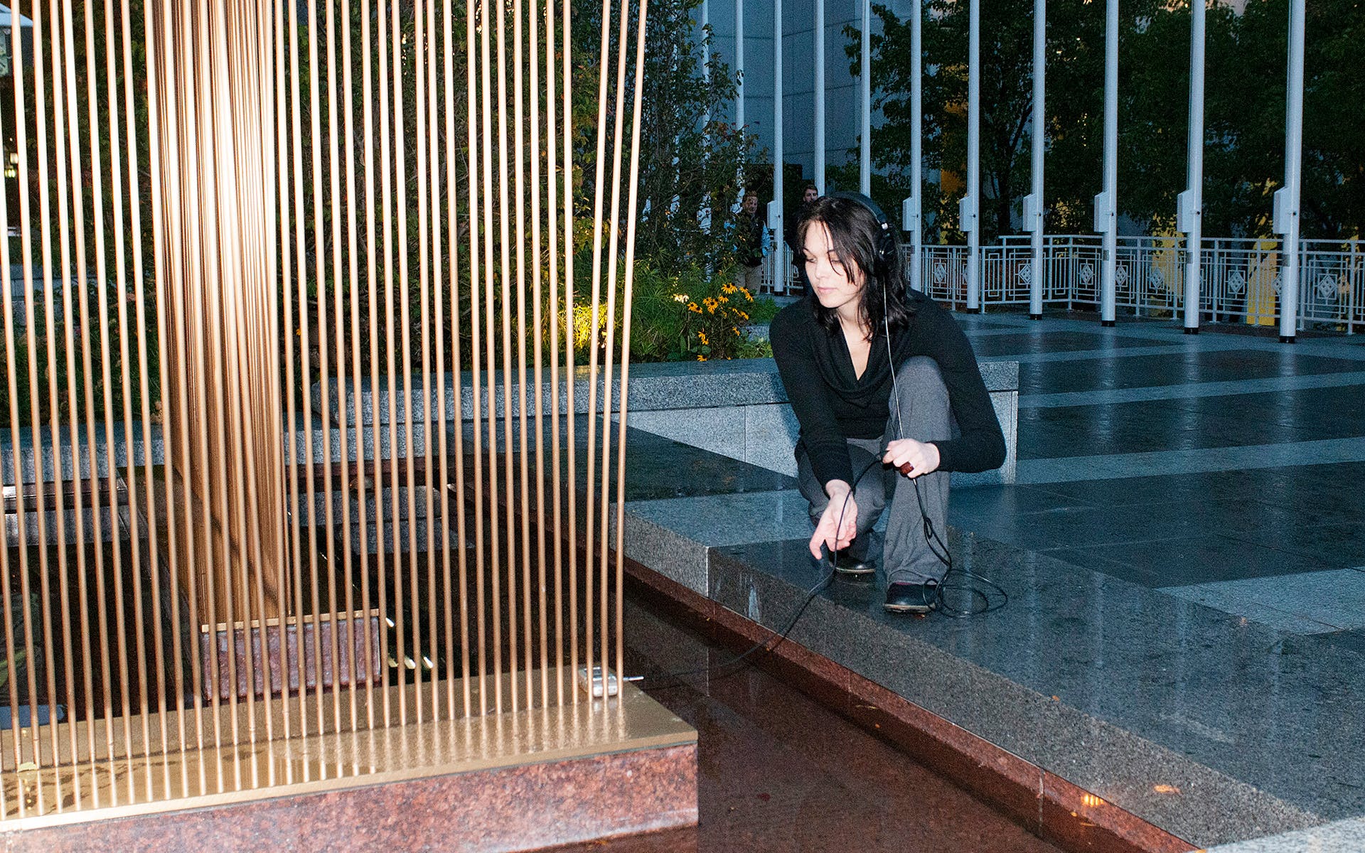 Woman leaning over metal sculpture listing to headphones.