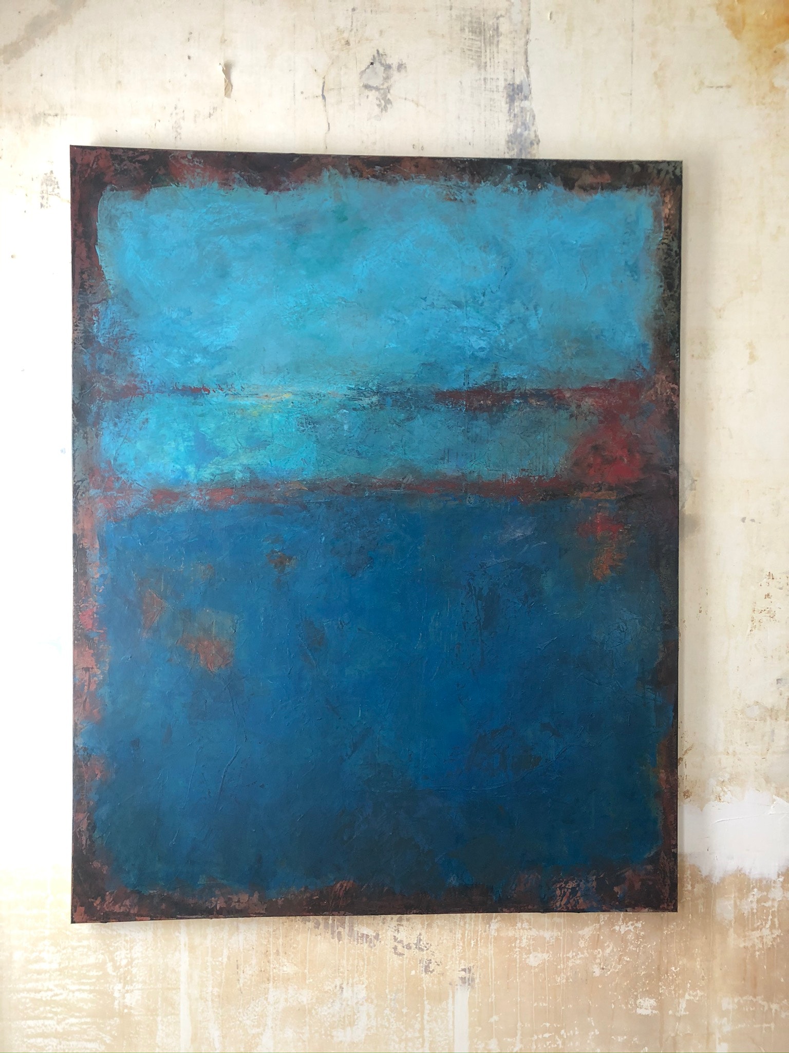 A rectangular painting; the bottom third is a dark blue and top third a lighter blue. The edges are a rusty brown, and all the paint has a blurred and uneven texture