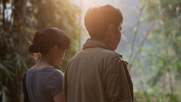 a woman and man stand beside one another in a wooded landscape.