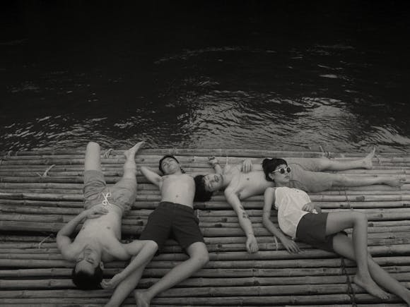 black and white image of a woman and three men lying on a dock.