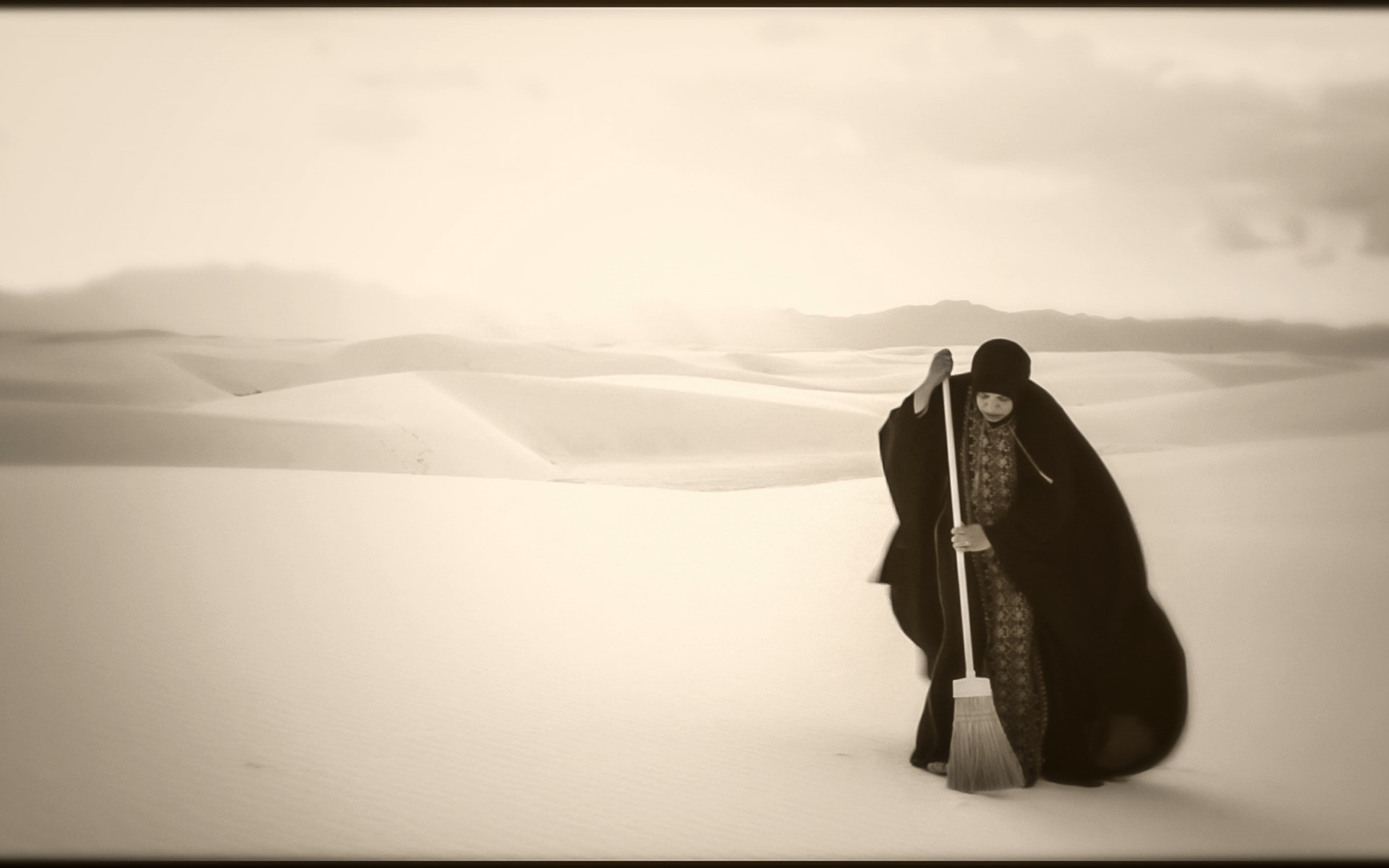 A woman sweeps a vast desert.