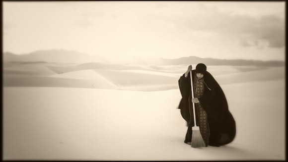 A woman sweeps a vast desert.