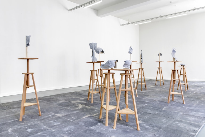 Image of a dozen sculptures featuring gray forms attached atop wooden stool tripod legs