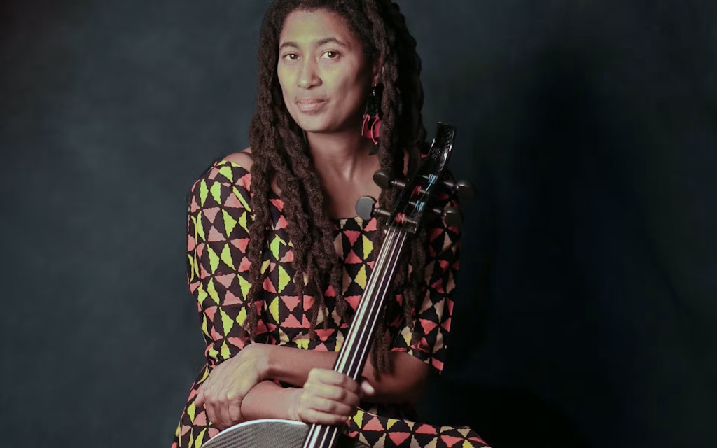 A medium-skinned adult looks at viewer holding a string instrument.