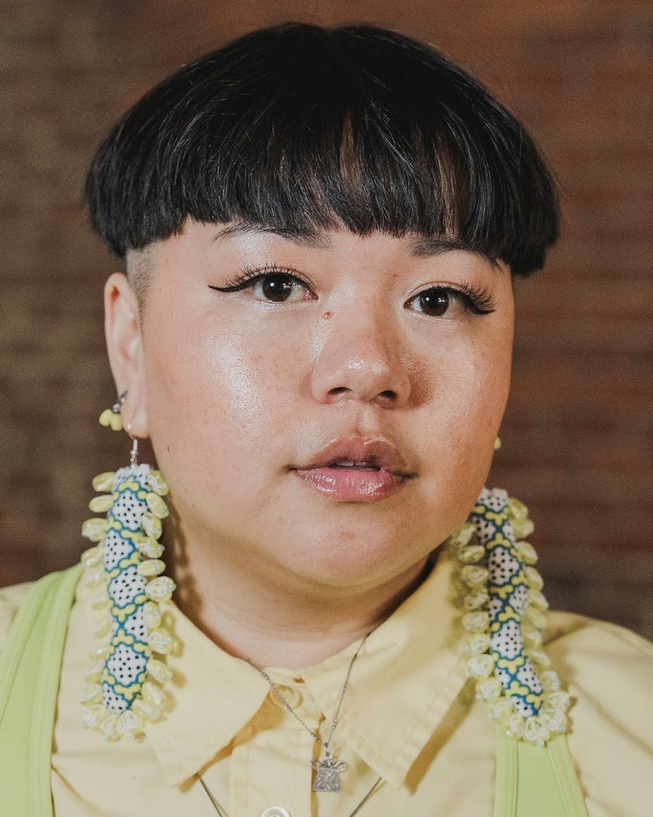 Headshot of a Hmong woman with very short dark hair, long beaded earrings, and a bright yellow shirt.