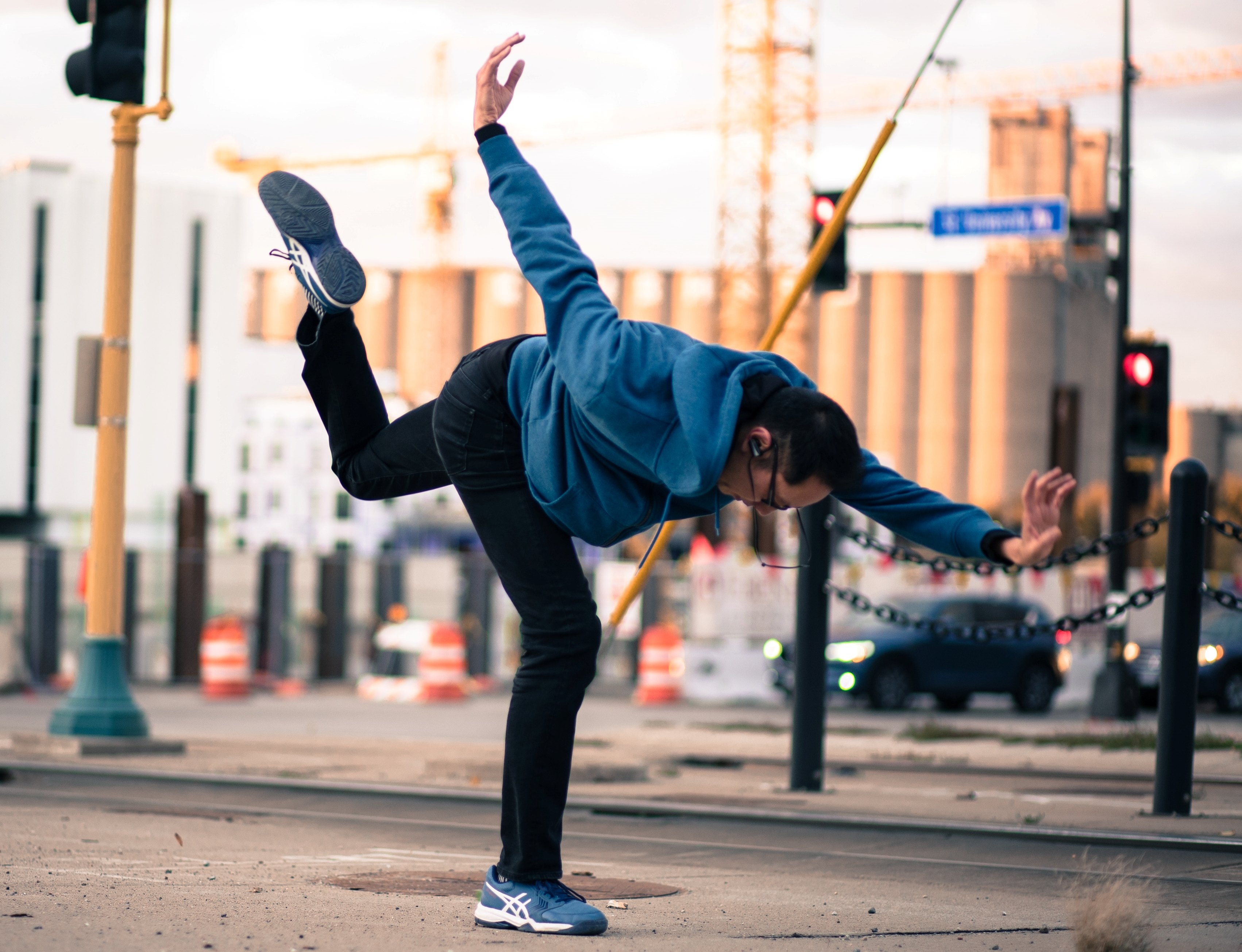 A man stands on one leg with the rest of his limbs pointed outward on a city street.