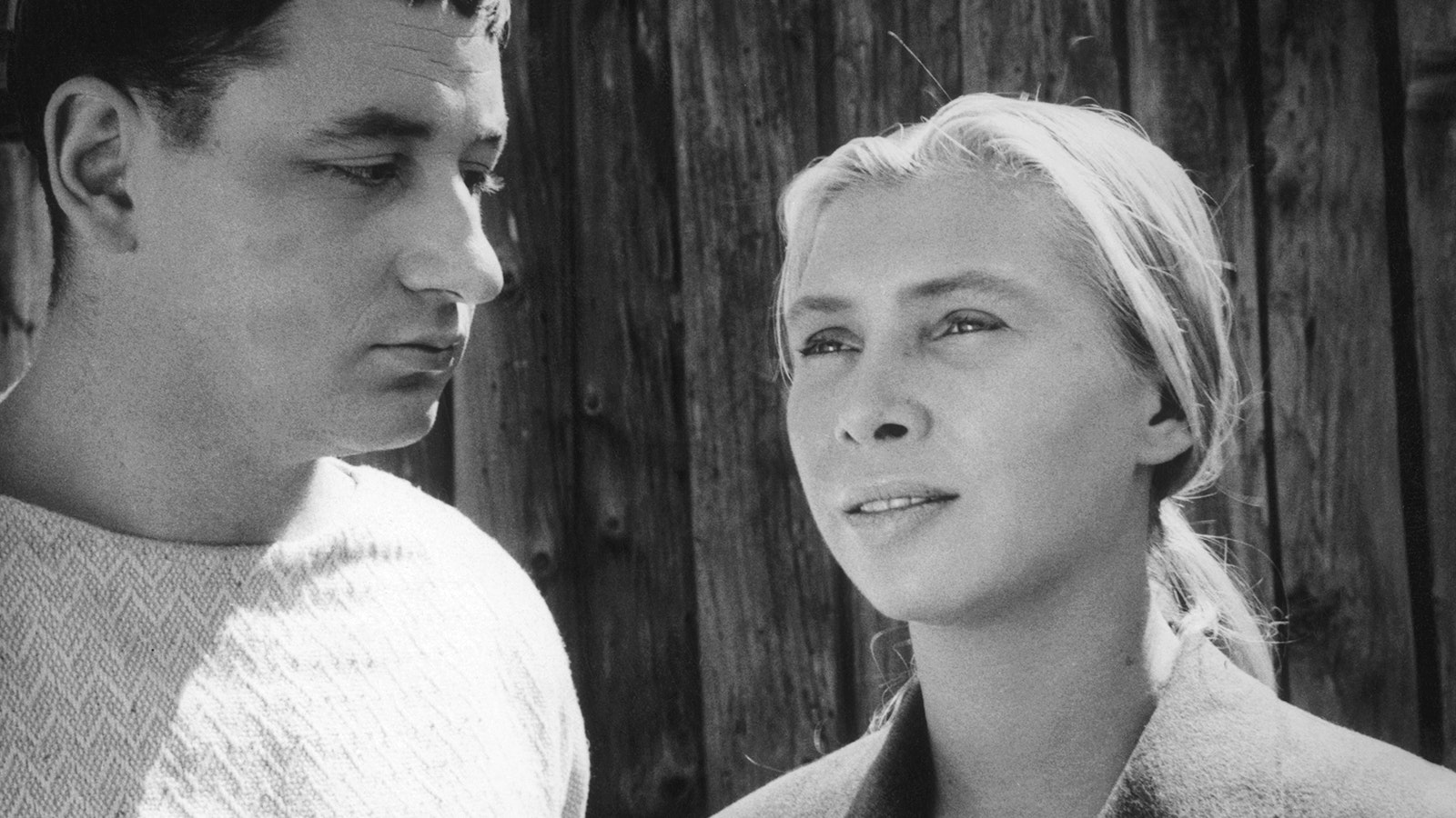 Black and white image two people – a woman with blond hair looking out and a man with dark hair looking at her.