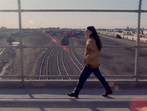 a woman walks across a bridge over train tracks.