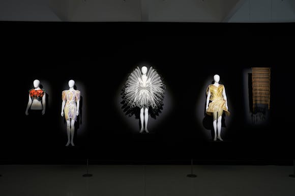 Four dresses on mannequins and one piece of cloth hung on a black wall